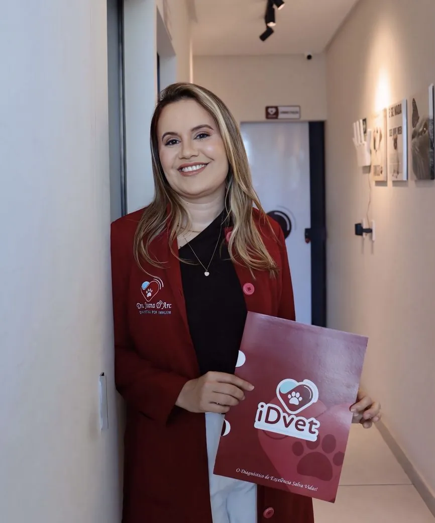 Dra. Joana D'Arc, responsável técnica do iDvet, no corredor da clínica segurando uma pasta do iDvet