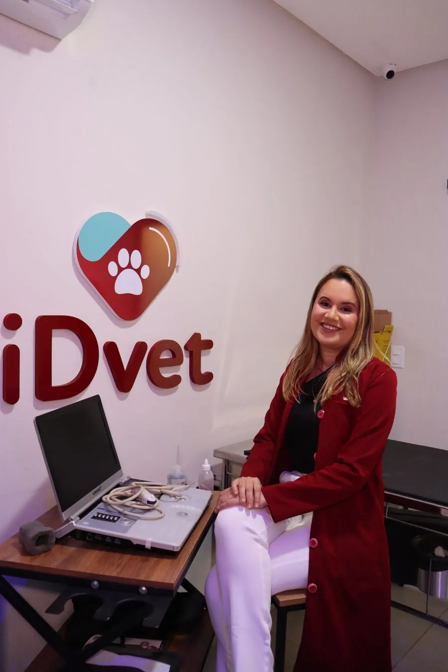 Médica Veterinária do iDvet sentada ao lado do aparelho de Ultrassonografia, na sala com a logo do iDvet