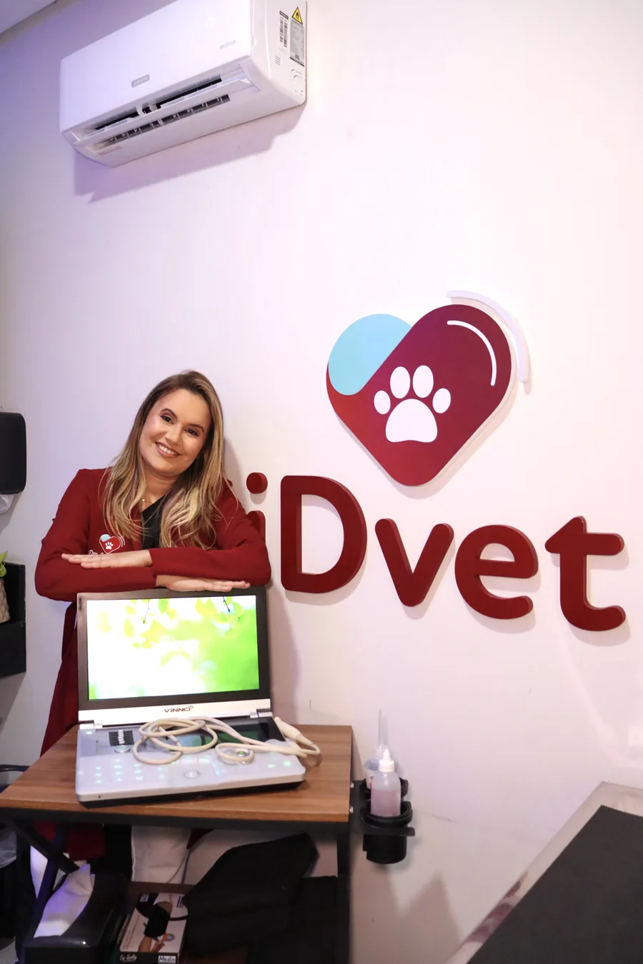 Médica Veterinária do iDvet ao lado do aparelho de Ultrassonografia, com a logo do iDvet na parede