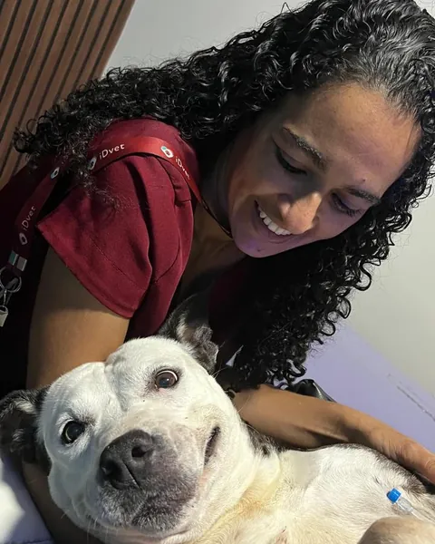 Cão de pelagem branca deitado, sorrindo, no colo de uma profissional do iDvet