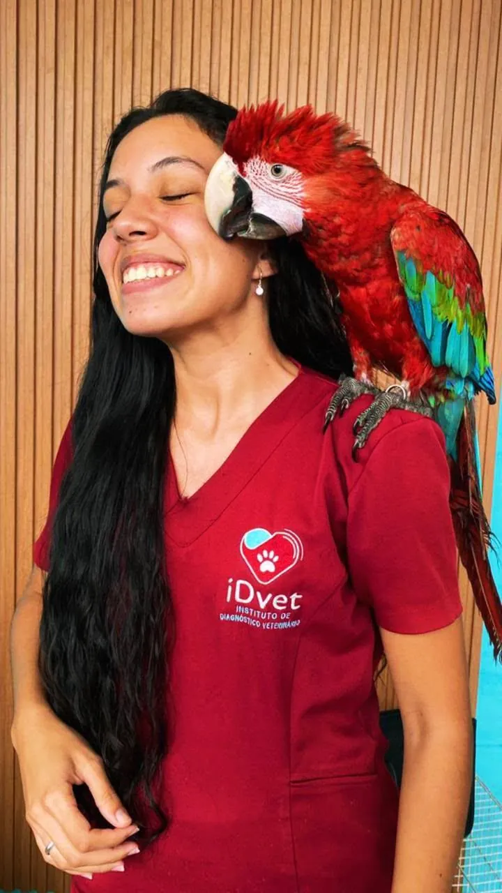 Médica veterinária do iDvet sorrindo com uma arara-vermelha no ombro